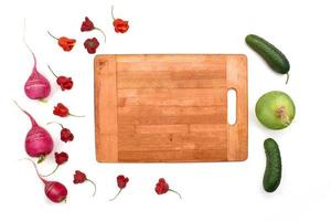 ingredientes para la preparación de ensaladas, almuerzos o cenas. rábano rosa y verde, pimiento rojo, pepino con tabla de cortar de madera sobre fondo blanco. copie el espacio foto