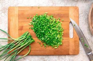 manojo picado de ajo verde en tabla de cortar de madera con cuchillo. Cocinando. ingrediente alimenticio. endecha plana foto