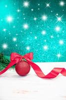 Christmas ball with pink bow and curled ribbon with spruce branches. Behind blurred green-blue background with stars. New Year. Vertical. Copy space photo
