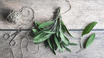 hojas de salvia atadas con hilo de cáñamo sobre una mesa de madera, hierbas planas, vista superior foto