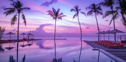 Fantasy dream outdoor infinity swimming pool with fantastic sunset clouds sky. Leisure summer vacation panorama. Travel landscape palm trees umbrellas water reflection. Colorful paradise islands beach photo