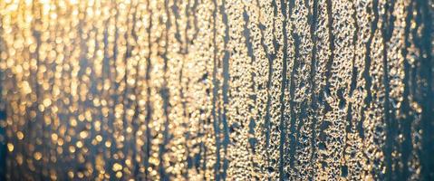 Texture of misted glass in winter. Frozen drops of water in sun on window. photo