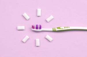 Toothbrush and chewing gums lie on a pastel pink background photo