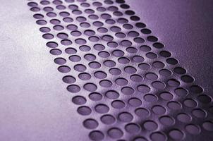 Black metal computer case panel mesh with holes on purple background. Abstract close up photo