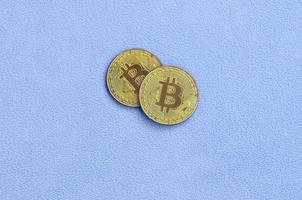 dos bitcoins dorados se encuentran sobre una manta hecha de suave y esponjosa tela de lana azul claro. visualización física de moneda criptográfica virtual foto