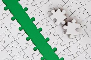 The green path is laid on the platform of a white folded jigsaw puzzle. The missing elements of the puzzle are stacked nearby. Texture image with space for text photo