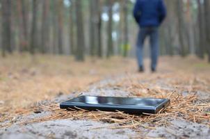 Young man loses his smartphone on Russian autumn fir wood path. Carelessness and losing expensive mobile device concept photo