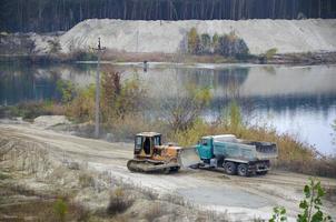 Caterpillar loader and dump truck works at the opencast mining quarry. Heavy machinery in the open pit at river. Dozer and truck on digging operations photo