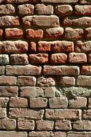 Vertical wall texture of several rows of very old brickwork made of red brick. Shattered and damaged brick wall with pinched corners photo