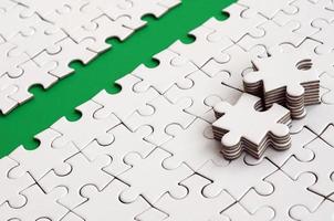 The green path is laid on the platform of a white folded jigsaw puzzle. The missing elements of the puzzle are stacked nearby. Texture image with space for text photo