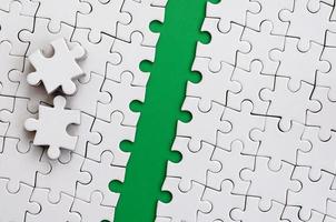 The green path is laid on the platform of a white folded jigsaw puzzle. The missing elements of the puzzle are stacked nearby. Texture image with space for text photo