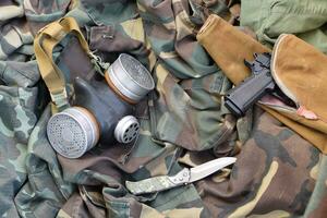 Stalker soldiers soviet gas mask lies with handgun and knife on green khaki camouflage jackets photo