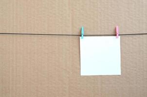 White blank card on rope on a brown cardboard background. Creative reminder, small sheet of paper on wooden clothespin, memo backdrop photo