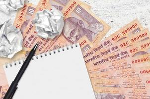 10 Indian rupees bills and balls of crumpled paper with blank notepad. Bad ideas or less of inspiration concept. Searching ideas for investment photo