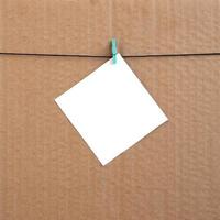 White blank card on rope on a brown cardboard background. Creative reminder, small sheet of paper on wooden clothespin, memo backdrop photo