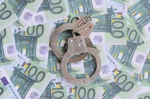 Police handcuffs lies on a set of green monetary denominations of 100 euros. A lot of money forms an infinite heap photo