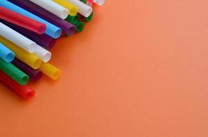 Many colorful straws for drinks lies on a bright orange background surface photo