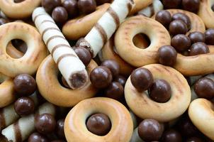 A lot of crispy sweet tubules, chocolate melting balls and yellow bagels lie on a wooden surface. Close up view photo