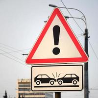 High risk of collision. A road sign with an exclamation point and two cars that crashed into each other photo