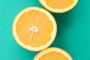 Top view of a several orange fruit slices on bright background in turquoise green color. A saturated citrus texture image photo