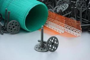 A set of construction items for the insulation of walls. Plastic dowels, a roll of mesh for the insulation of facades and a corner profile with a grid lie on the foam polystyrene surface photo