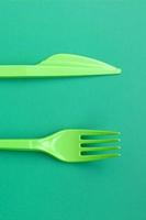 Disposable plastic cutlery green. Plastic fork and knife lie on a green background surface photo