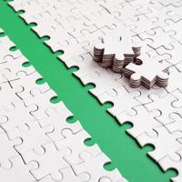 The green path is laid on the platform of a white folded jigsaw puzzle. The missing elements of the puzzle are stacked nearby. Texture image with space for text photo