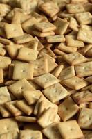 A lot of small cookies are square shaped. A pattern of a yellow salt cracker. Background image with salted pastry photo