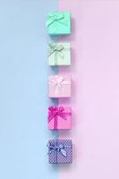 Small gift boxes of different colors with ribbons lies on a violet and pink background photo