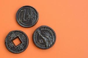 Three chocolate products in the form of Euro, USA and Japan coins lie on an orange plastic background. A model of cash coins in an edible form photo