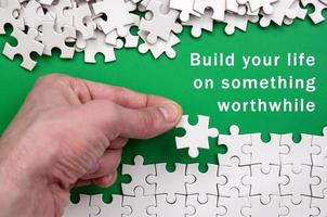 Build your life on something worthwhile. The hand folds a white jigsaw puzzle and a pile of uncombed puzzle pieces lies against the background of the green surface photo