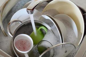 platos sucios y electrodomésticos de cocina sin lavar yacen en agua de espuma bajo un grifo de cocina foto