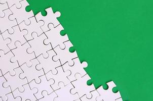 Fragment of a folded white jigsaw puzzle on the background of a green plastic surface. Texture photo with copy space for text