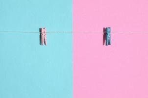Two colored wooden pegs and small rope lie on texture background of fashion pastel blue and pink colors paper in minimal concept photo