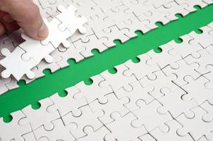 The human hand paves the way to the surface of the jigsaw puzzle, forming a green space. The concept of overcoming the difficulties on the way to success photo