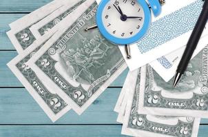 2 US dollars bills and alarm clock with pen and envelopes. Tax season concept, payment deadline for credit or loan. Financial operations using postal service photo