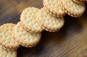 A round sandwich cookie with coconut filling lies in large quantities on a brown wooden surface. Photo of edible treats on a wooden background with copy space