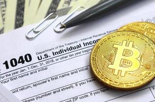 The pen, bitcoins and dollar bills is lies on the tax form 1040 U.S. Individual Income Tax Return. The time to pay taxes photo