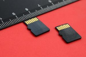 Two small micro SD memory cards lie on a red background next to a black ruler. A small and compact data and information store photo