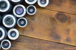 Several photographic lenses lie on a brown wooden background. Space for text photo