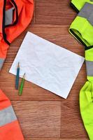 una hoja de papel arrugada con dos lápices rodeada de uniformes de trabajo verdes y naranjas foto