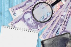 100 billetes de piso filipino y lupa con monedero negro y bloc de notas. concepto de dinero falso. busque diferencias en los detalles de los billetes de dinero para detectar falsos foto