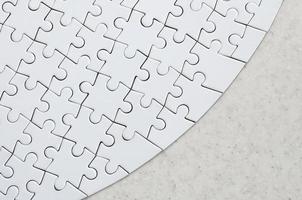 A white jigsaw puzzle in the complete form lies on a treated stone surface. Textured image with copy space photo