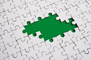 Close-up texture of a white jigsaw puzzle in assembled state with missing elements forming a green pad for text. Copy space photo