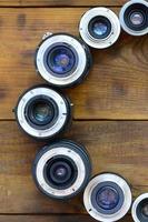 Several photographic lenses lie on a brown wooden background. Space for text photo