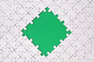 Framing in the form of a rhombus, made of a white jigsaw puzzle around the green space photo