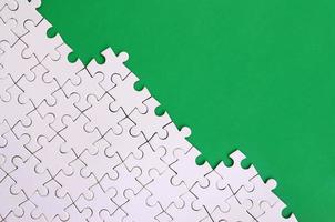 Fragment of a folded white jigsaw puzzle on the background of a green plastic surface. Texture photo with copy space for text