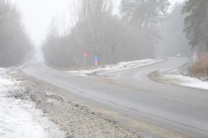 cruce de caminos en una carretera asfaltada suburbana en invierno durante una ventisca foto