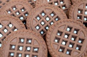 Detailed picture of dark brown round sandwich cookies with coconut filling close up. Background image of several treats for tea photo