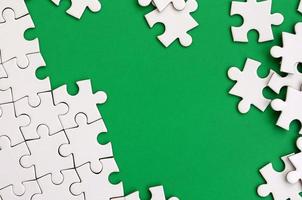 Fragment of a folded white jigsaw puzzle and a pile of uncombed puzzle elements against the background of a green surface. Texture photo with space for text